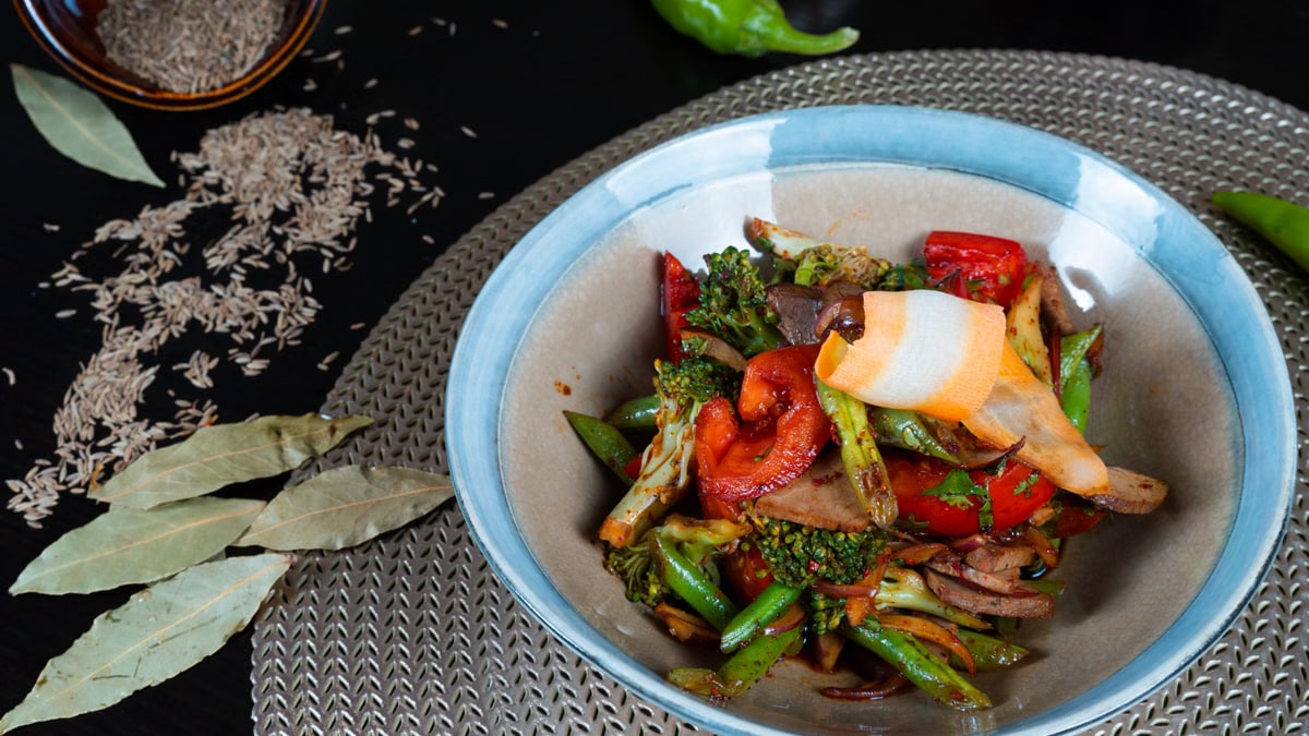 A vibrant vegetable stir-fry in a bowl, surrounded by spices and herbs, ready for a healthy meal.